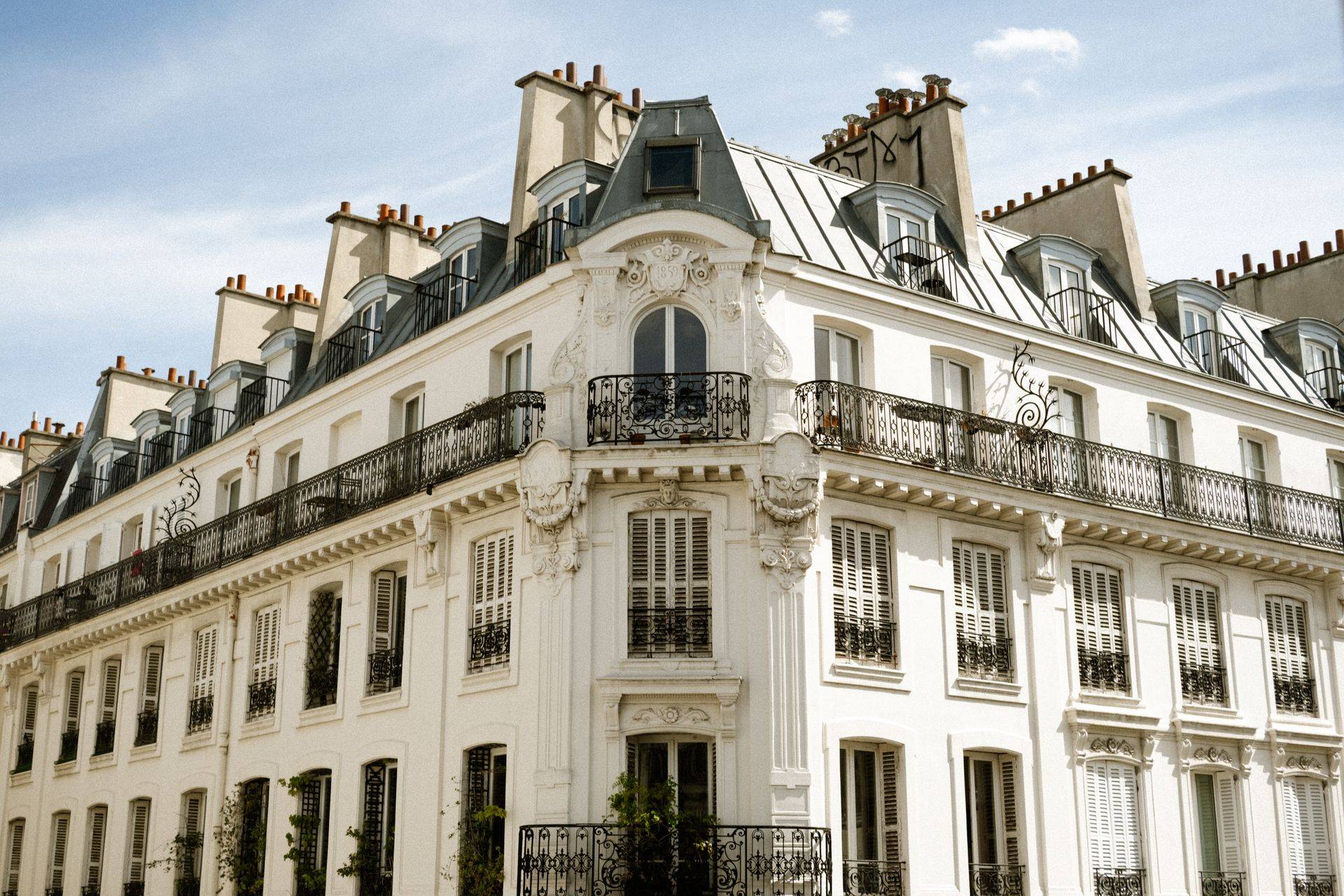 Façade d'immeuble parisien en pierre claire avec balcons en fer forgé, au soleil